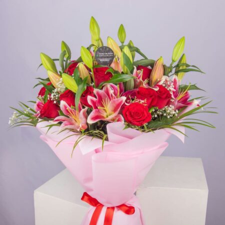 A bouquet of lilies and roses in a nice pink wrapping and tied with a red ribbon