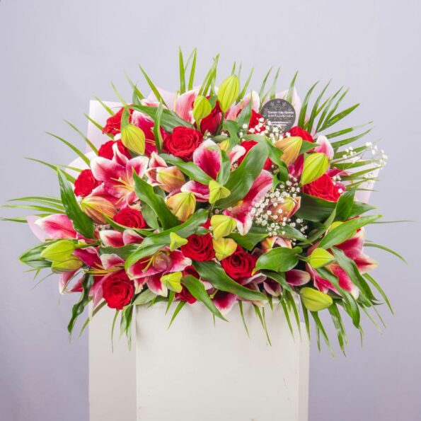 A bouquet of lilies and roses in a nice pink wrapping and tied with a red ribbon