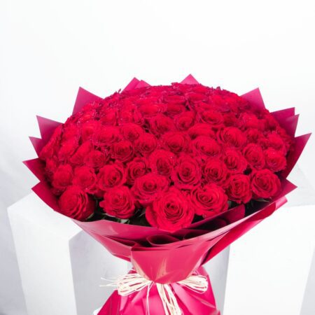 Close-up view of Gift-ready bouquet of 101 premium red roses, elegantly wrapped in rustic red paper and adorned with a natural raffia knot