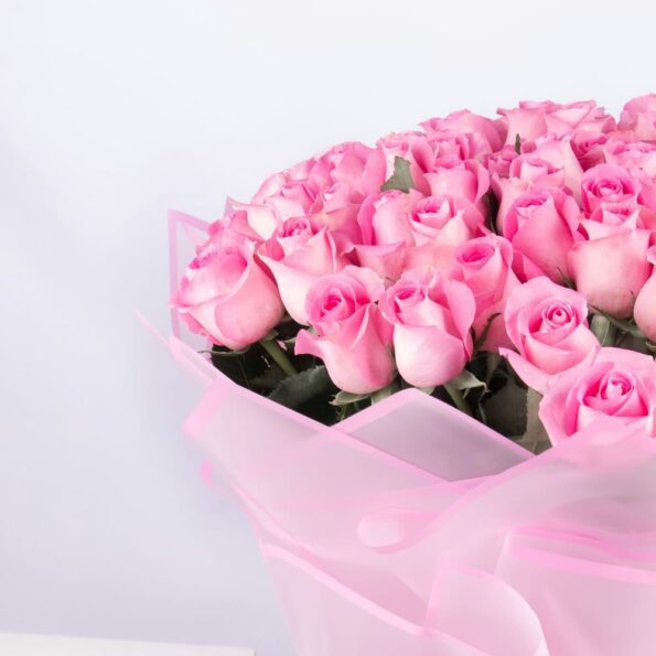 Close-up of a 101 pink rose bouquet, showcasing the vibrant blooms, eco-friendly pink paper wrapping, and delicate pink ribbon