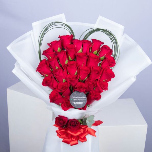 Bouquet of red roses wrapped in white paper with a heart in the middle.