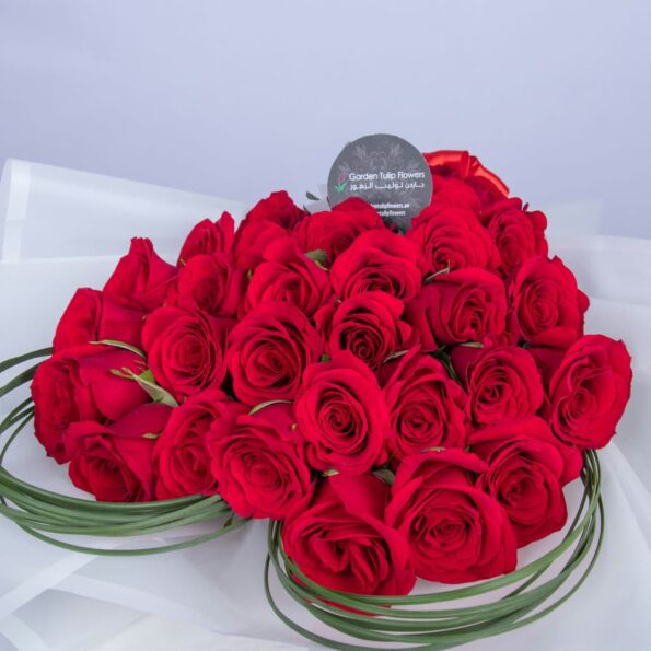 Bouquet of red roses wrapped in white paper with a heart in the middle.
