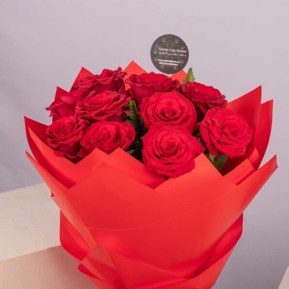 A bouquet of red roses wrapped in red paper, tied with a red ribbon