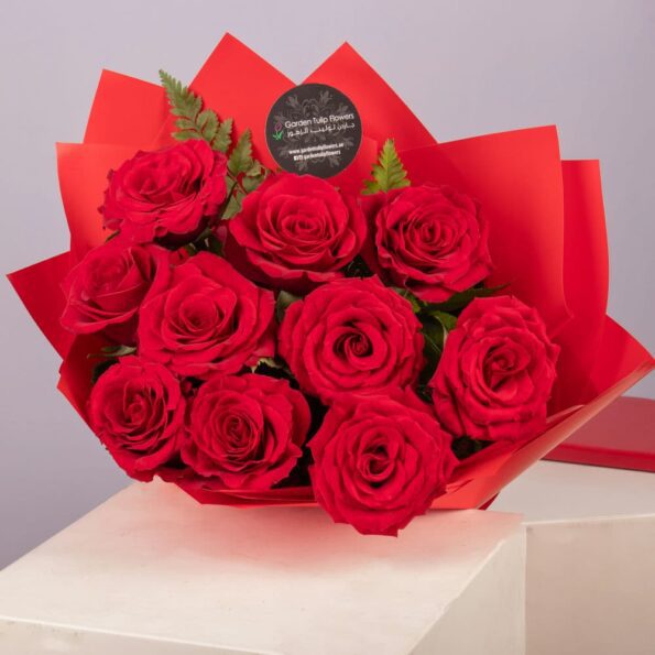 A bouquet of red roses wrapped in red paper, tied with a red ribbon