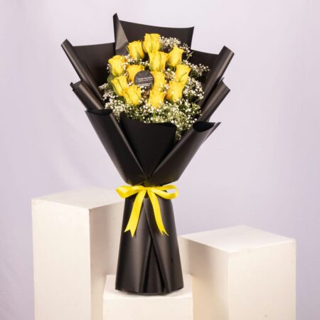 A bouquet of yellow roses wrapped in black paper with a yellow bow