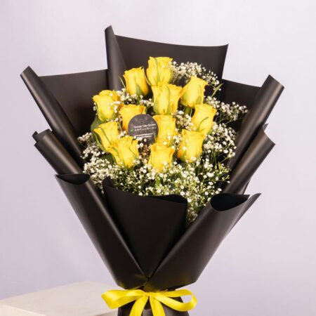 A bouquet of yellow roses wrapped in black paper with a yellow bow