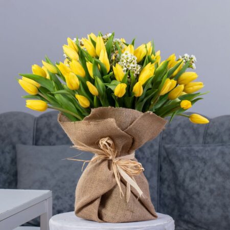 A bouquet of yellow tulips with baby breath wrapped in a burlap bag