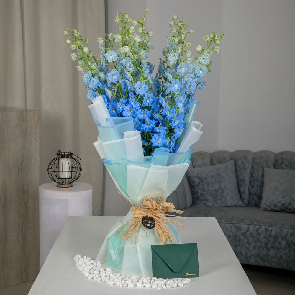 A bouquet of blue delphiniums with a green envelope and card on a table
