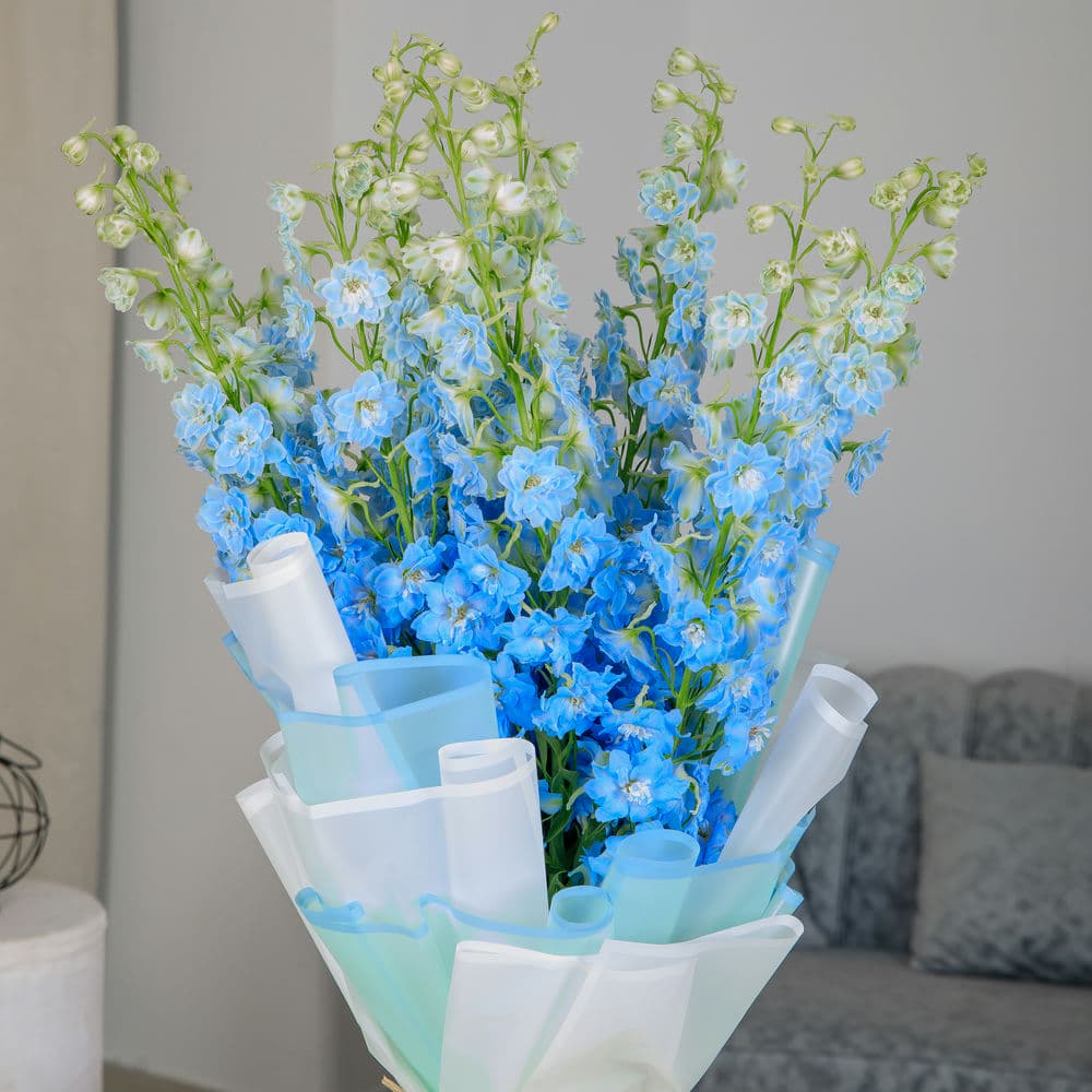 close up blue delphiniums bouquet with a green envelope and card on a table