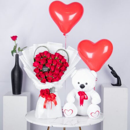 Red Roses arranged in a Heart Shape with Steel Grass, heart shaped balloons and a White Teddy Bear