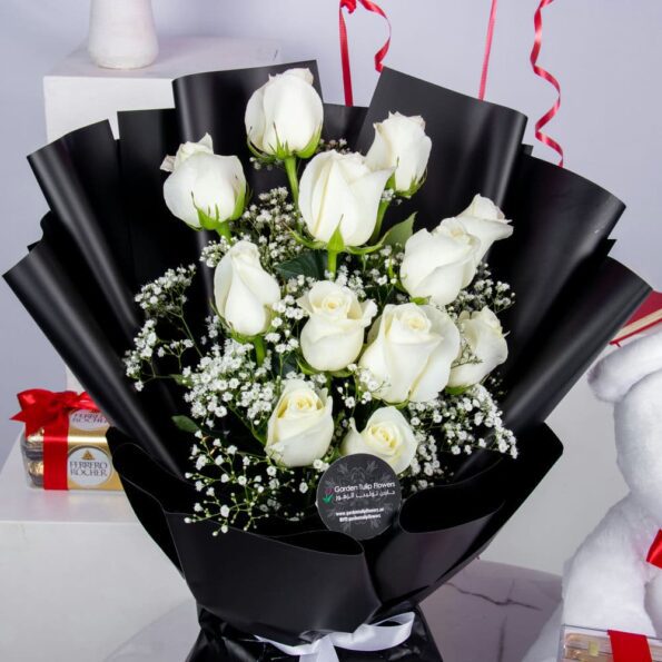 A bouquet of white roses, a box of chocolates, a teddy bear, & two heart-shaped balloons