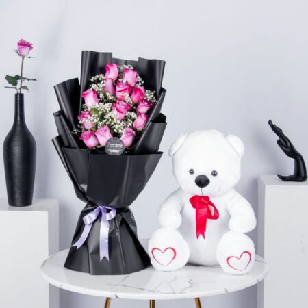 A bouquet of pink roses in a nice black wrapping with teddy bear