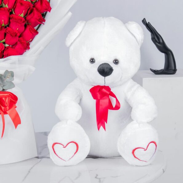 A close-up view of white teddy bear with rose bouquet