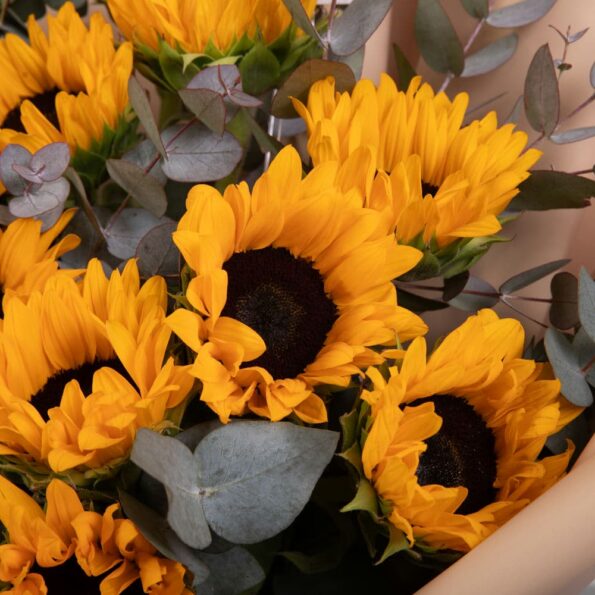 close up view of bouquet of sunflowers wrapped in brown paper with a card